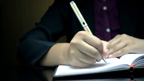 Businesswoman's hand signing document. Close-up of human hand writing on a paper.