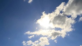 Time lapse clip of white fluffy clouds over blue sky and sun
