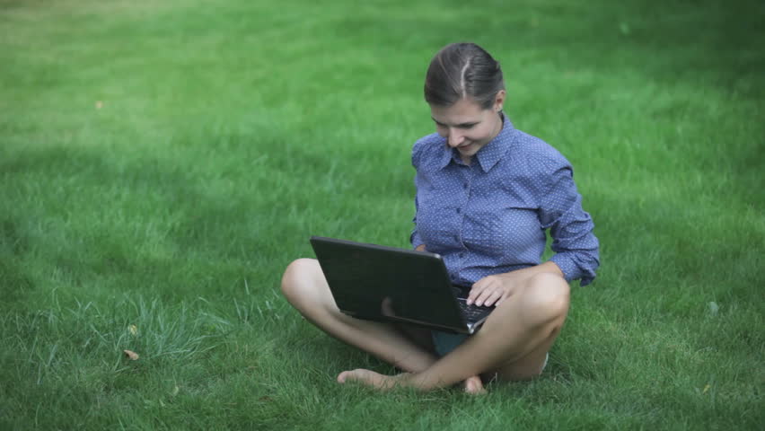 Young woman sitting in pose lotus and typing letter outdoor