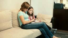 Mom and daughter sitting on sofa watching video on smartphone