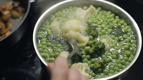 Close up of cooking colorful broccoli, pea and cauliflower in the pot with boiling water in kitchen at home. Slow motion. Vegetarian food. Raw vegetable food. Healthy nutrition diet and weight loss