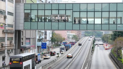 HONG KONG - APRIL 13, 2017: Convenient pedestrian and auto traffic separation in Hong Kong. People go inside enclosed skybridge above Kwai Chung Road, vehicles rush on throughway, overpass ahead