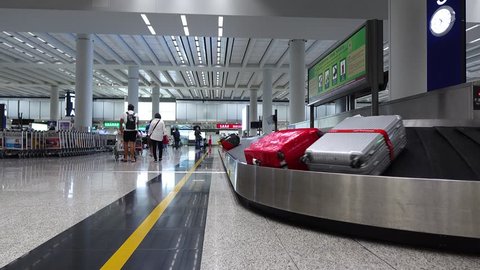 Few large bags move on conveyor belt, luggage claim hall of modern airport, rather empty space. Two people come away, baggage carousel turn ahead. Hong Kong International airport arrival area