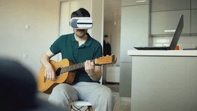 Happy young man sitting at kitchen learning to play guitar using VR 360 headset and feels him guitarist at concert at home