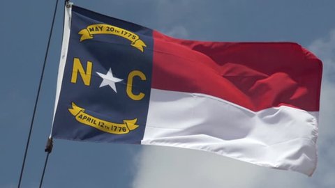 An extreme 180-fps slow motion establishing shot of the North Carolina state flag blowing in the breeze.  	