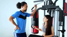 Video footage of a young woman talking with her Afro trainer while sitting on a gym equipment