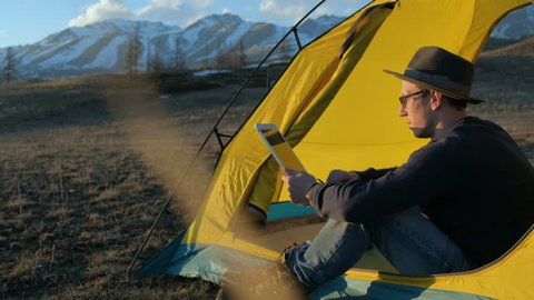 Handsome young man tourist using cell phone and portable mini speaker in touristic tent 20s 4k Stock-video
