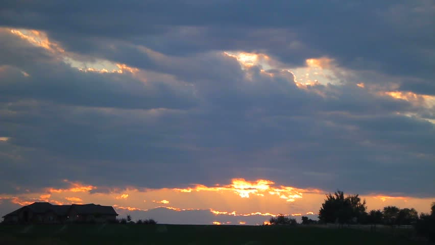 Sunset with clouds passing over pasture and farm house.
