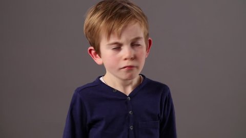 free little 6-year old boy shaking his head and swinging his arms to express his refusal, boredom or happy disagreement, grey background studio