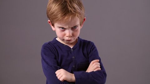 conflicted little 6-year old red hair child with arms crossed and dirty look showing his profile to express his frustration with an offended body language, grey background studio
