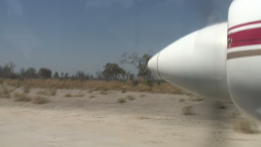 A closeup shot through the propeller of an airplane taking off from a dirt