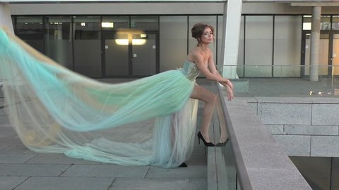 Beautiful girl standing on the balcony, she was wearing a gentle blue dress that develops in the wind, a very long dress.