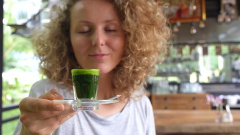 Young Healthy Woman Holding Wheatgrass Shot With Thumbs Up in Vegetarian Restaurant. Healthy Lifestyle Concept. Slow Motion.