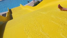 Little 8 year old child cheerfully slides down yellow waterslide in pool on sunny summer day. Real time full hd video footage.