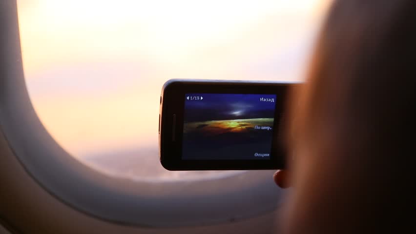 Closeup of mobile phone in hands of cute funny kid taking pictures of beautiful sunset sky in plane during flight. Child of 9 years sits on his seat near window. Real time full hd video footage.