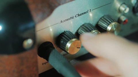 Women's hands twist tumblers on control panel of guitar amplifier. A mode switch being switches on amp. Man's hand inserts cable jack in guitar amp
