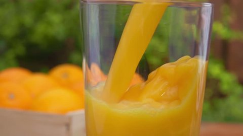 Orange juice is poured into a glass on a background of a box of ripe oranges. close-up camera motion