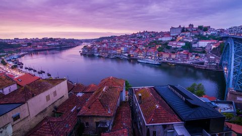 Amazing Porto Timelapse at sunset, old city with river Douro in the foreground. Boats passing by with the Arrabida bridge in the distance and the Dom Luis bridge on the right turning on the lights. 