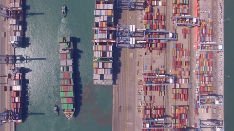 Aerial time lapse of a Commercial port with container ships during loading and unloading, and a container ship pulled by tugboats - Top down aerial view.