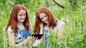 Two cool twins girls are listening to music outdoors. Beautiful red hair, smiling, having a good time. 4K slow motion video