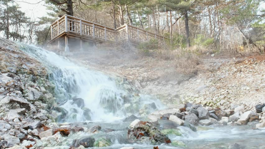 Waterfall from hot spring sources collected into a pool and hot water running down the valley in a warm stream in Kusatsu Onsen,Sainokawara Park hot spring, Japan