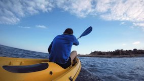Active and dynamic POV shot from water of a fit healthy strong man in blue active wear paddling a yellow adventure kayak to the safety of shore, on holiday summer destination