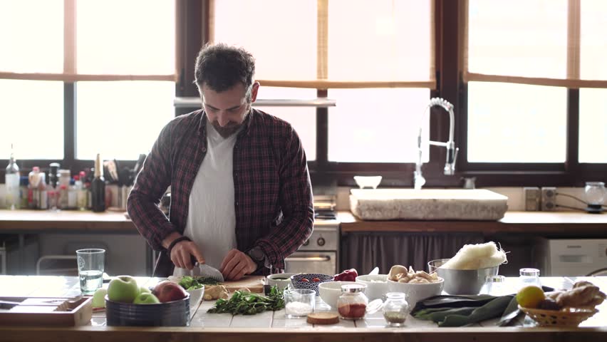 Funny happy couple cook dinner in an open space kitchen full of light, he is serious chops organic vegetables and she tries to steal a snack. they are excited, peaceful and loving Royalty-Free Stock Footage #26995495