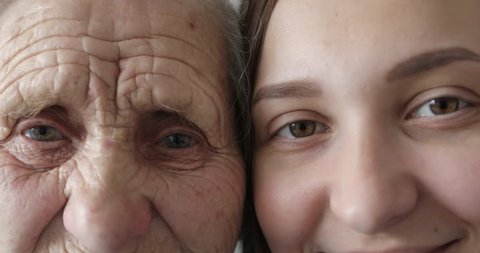 Old and young face. Grandmother and granddaughter looking together at camera. Close-up. 4K.