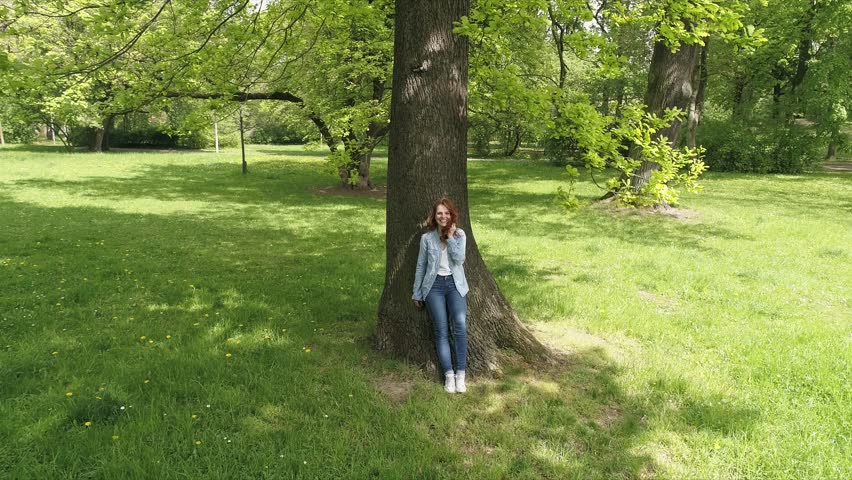 woman relaxing leaning against a tree trunk in the park