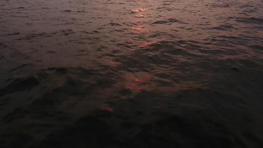 Cinematic forward flight above flat sea waves water camera tilts to horizon with round red sun. Vladivostok Russia city skyline panorama. Aerial drone 4k footage. Summer sunrise.