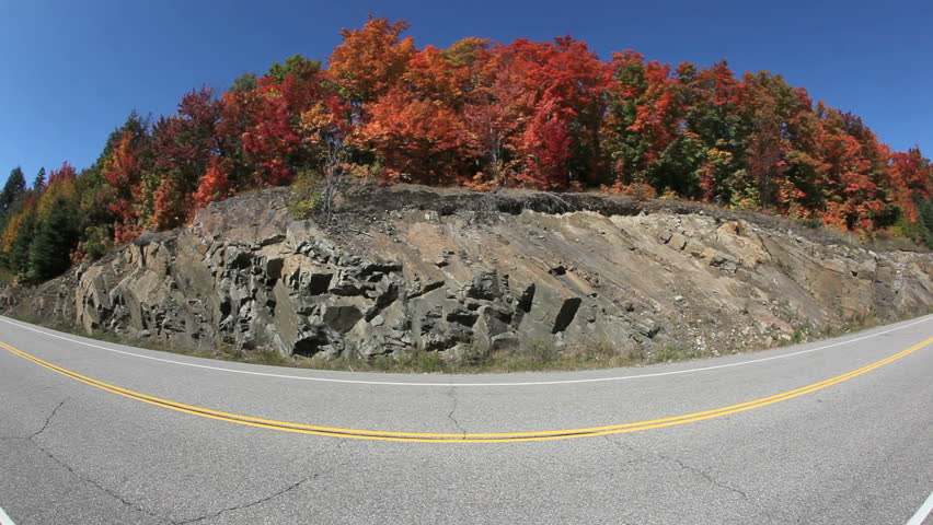 Cars passing by on a highway in fisheye view with fall colors in the background