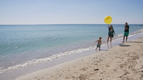 Gorgeous little boy having fun summer time with his family on the sunny beach, running with big yellow balloon on the sea coast. Slow motion.