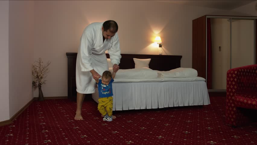 Dad teaches a child to walk in a hotel room