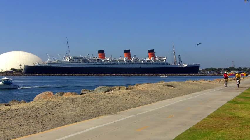 LONG BEACH, CA - AUGUST 5: A young couple ride bicycles with the Queen Mary in