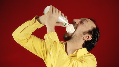A funny man sprays whipped cream directly into his mouth. Medium close-up shot.
