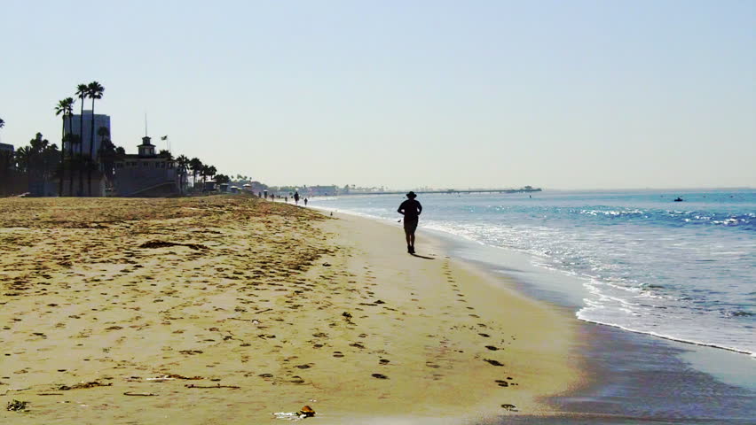 A mature man jogs on a Southern California beach toward the camera. 