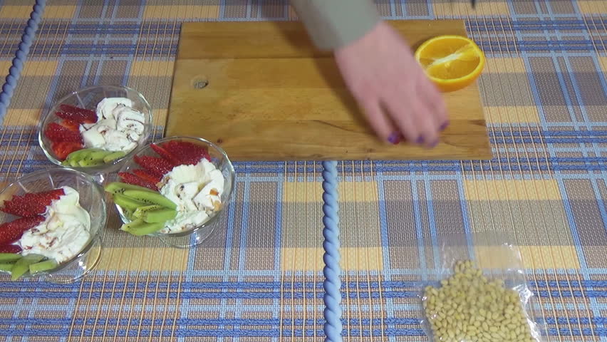 The girl cuts an orange and puts it in a cup of vanilla ice cream. Raspberry berries lie on the cutting board. Whipped cream. A metal knife. Food video. Waffle cup.