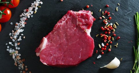 Beautiful juicy fresh meat steak on a table with salt, rosemary, garlic, and tomato on a black background, top view. Concept: fresh & natural products, bio products, meat products, organic, nutrition.