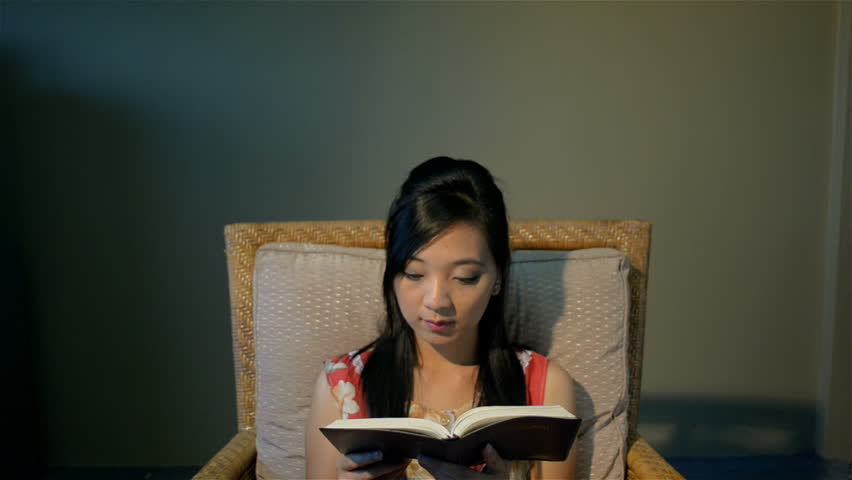 Young Asian woman relaxing on a chair, reading the bible/ a book - tracking into