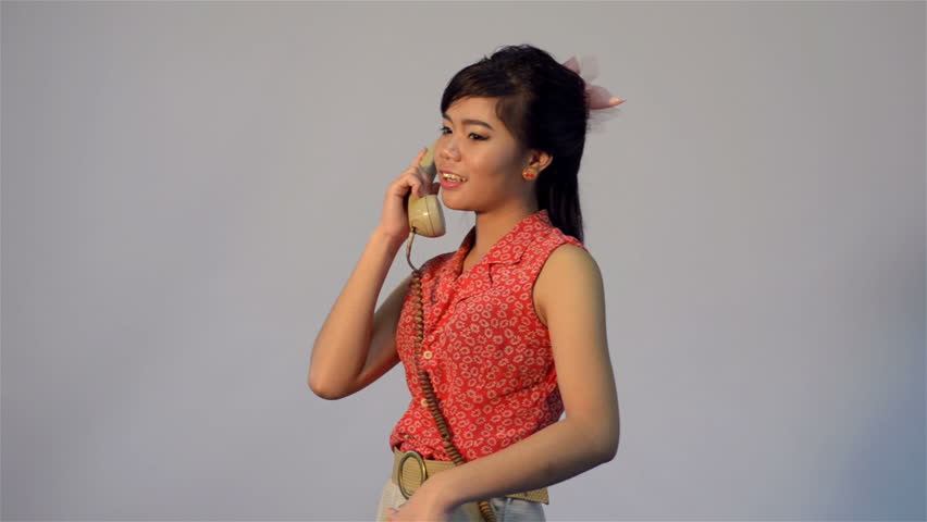 Vintage dressed young Asian woman happily talking on the phone - tracking shot.