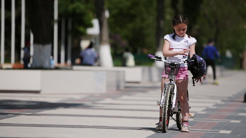 Cute girl wearing helmet and then rides a bicycle in park in sunshine day.