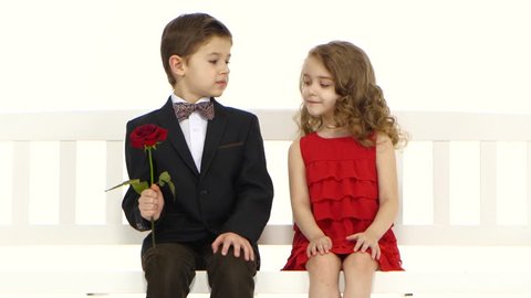 Little boy gives a rose to his girlfriend and kisses her on the cheek. White background