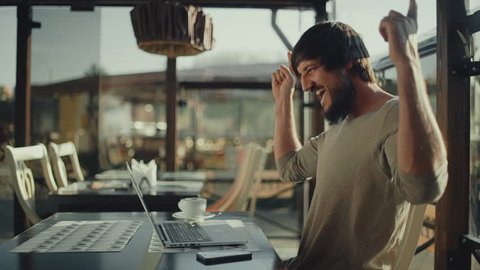 Bearded man freelancer very happy and rejoices sitting in front of laptop in cafe