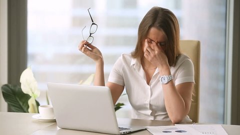 Young businesswoman taking off glasses while working on laptop at office, feeling discomfort and eye strain after long wearing, massaging nose bridge, blurry irritated dry eyes, eyesight problems 