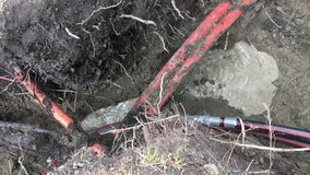 Burying high voltage electrical cable underground with clip capturing cable moving underground up to large wooden spool where it's being unraveled. 