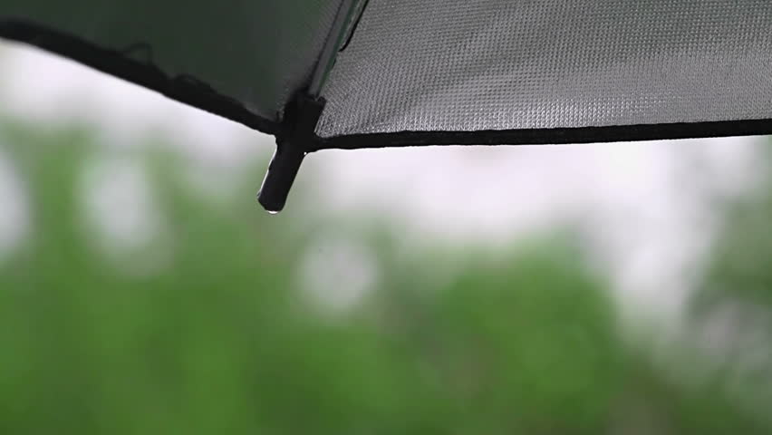 Rain coming down on silver umbrella and making drops of water falling off the