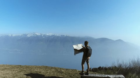 Aerial shot of hiker looking at map from mountain top. Man reaches mountain top, looks at map for directions. People travel concept.