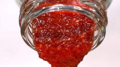 Ketchup or Red Sauce is Pouring out from a Glass Bottle Macro in Slow Motion White Background Tabletop 