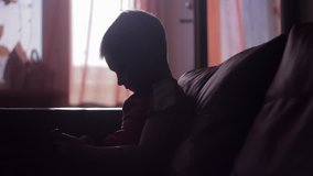 Silhouette of a young boy playing game on smartphone in home