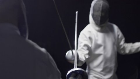 Two opponents in protective masks and costumes practicing fencing fight. Slow motion shot